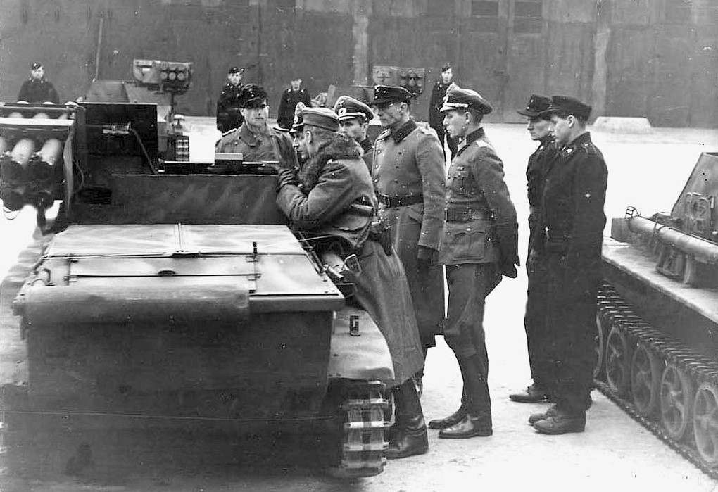 German officers inspecting a Kleinpanzer Wanze unit, the young crew in black stand nearby.